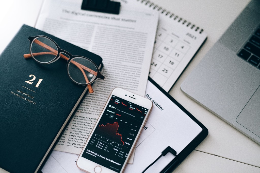 Finance professional reviewing market data on phone with journal and laptop